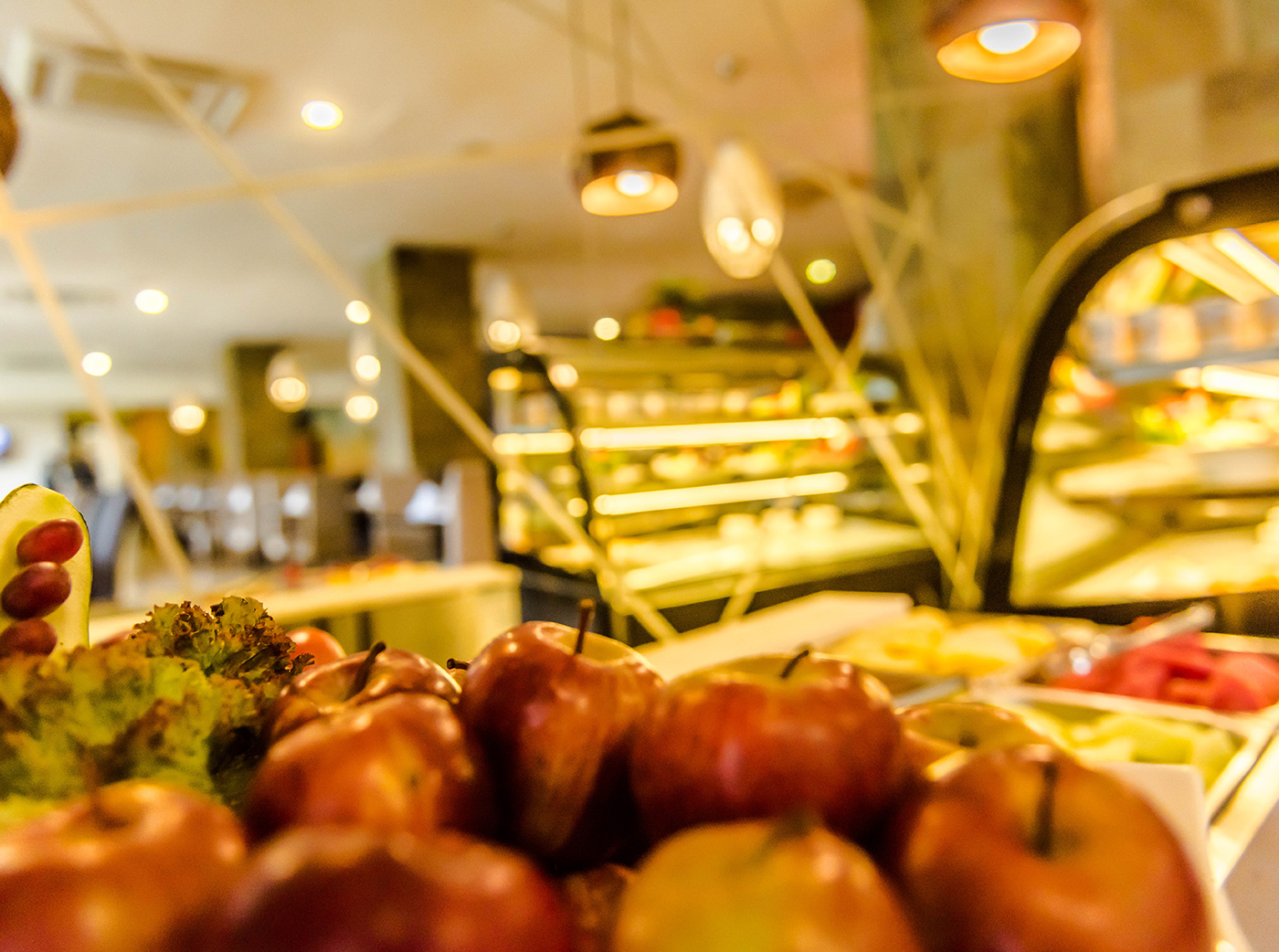 Close-up of fresh apples and fruit on display with a blurred buffet counter in the background, warm golden lighting
