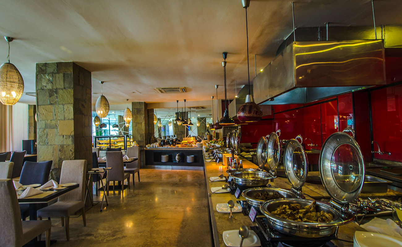 Restaurant interior with dining tables, chairs, and a buffet counter with chafing dishes and hanging woven lamp shades, warm inviting mood