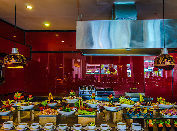 Buffet spread of garnished salads and dishes on a table under a red-lit backdrop with hanging lamps